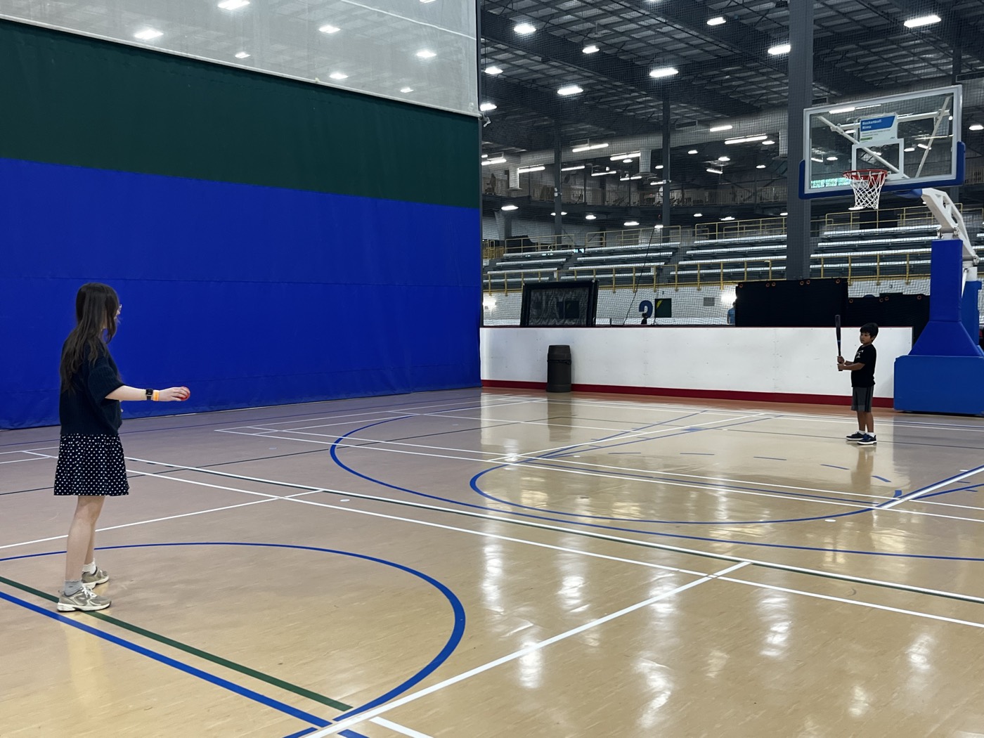 Two children playing catch with a bat and ball in an indoor gym
