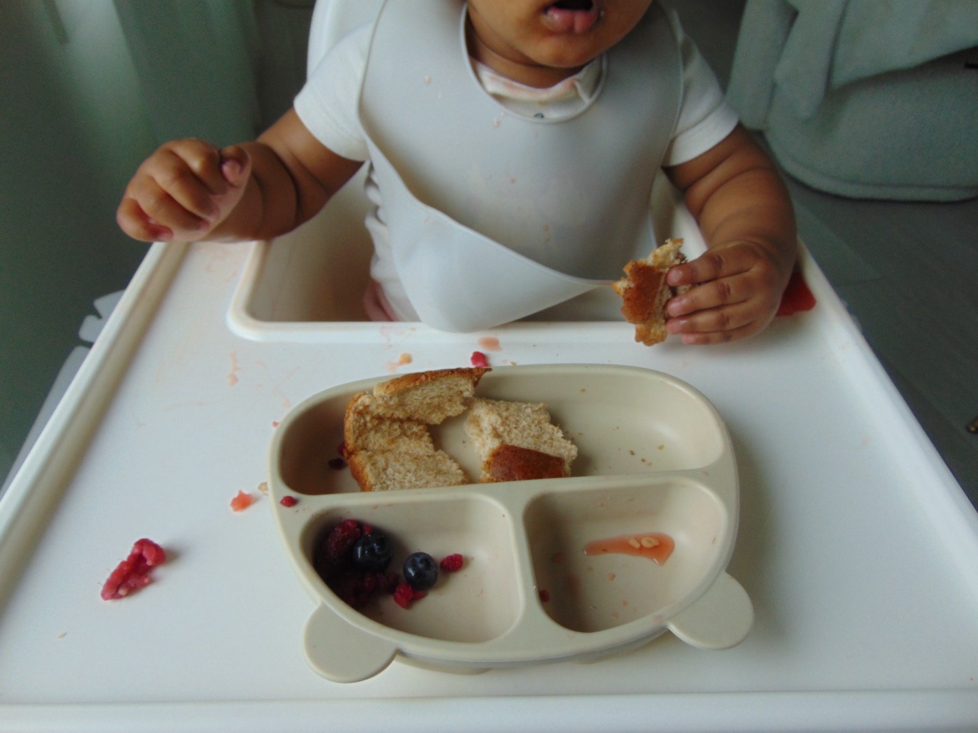 A baby in a high chair with bread and fresh berries on a plate
