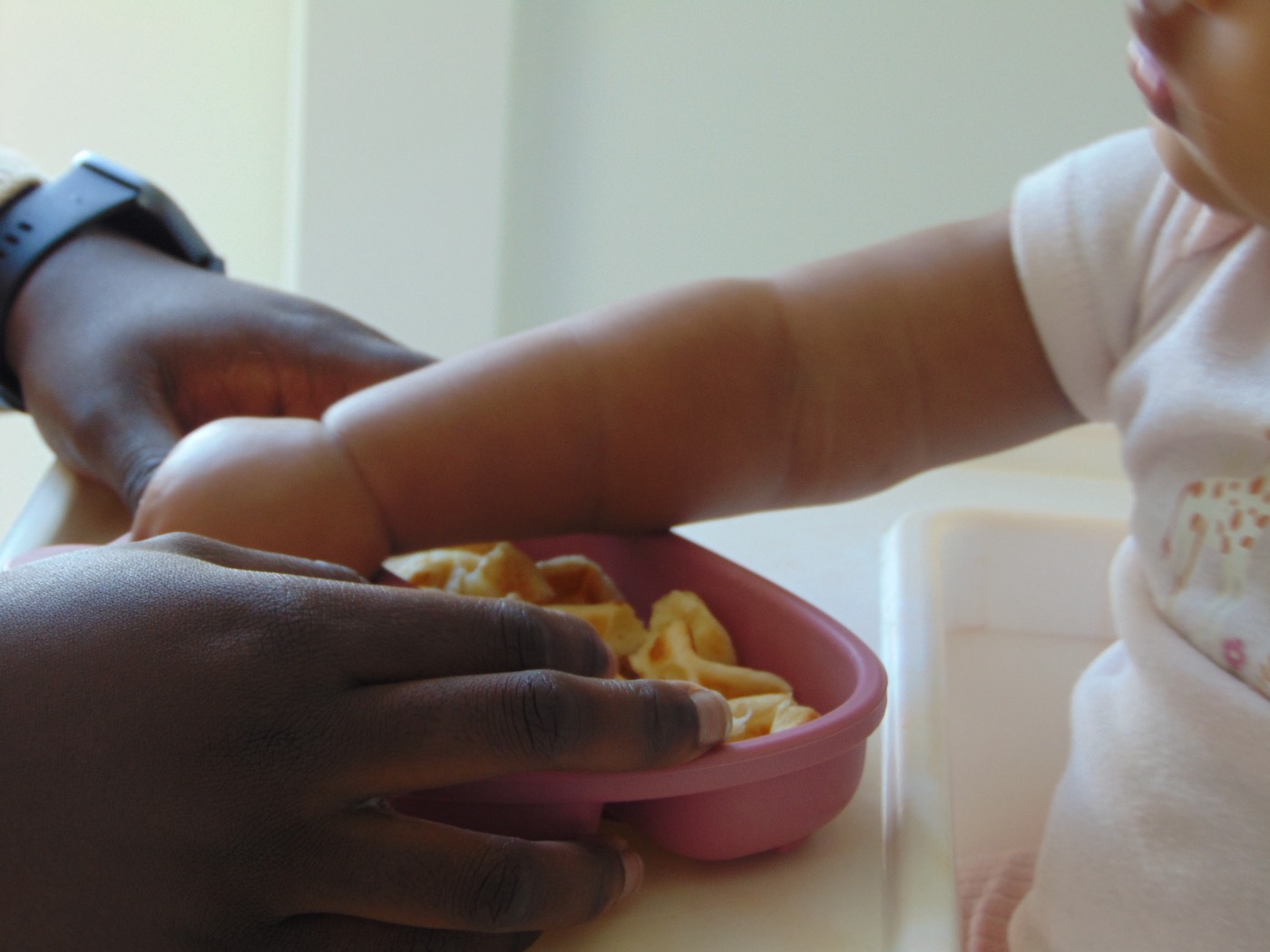 A caregiver offering a bowl of food to a baby at the table